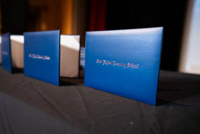 Blue diplomas lined up on a black table, reflecting the ambient light