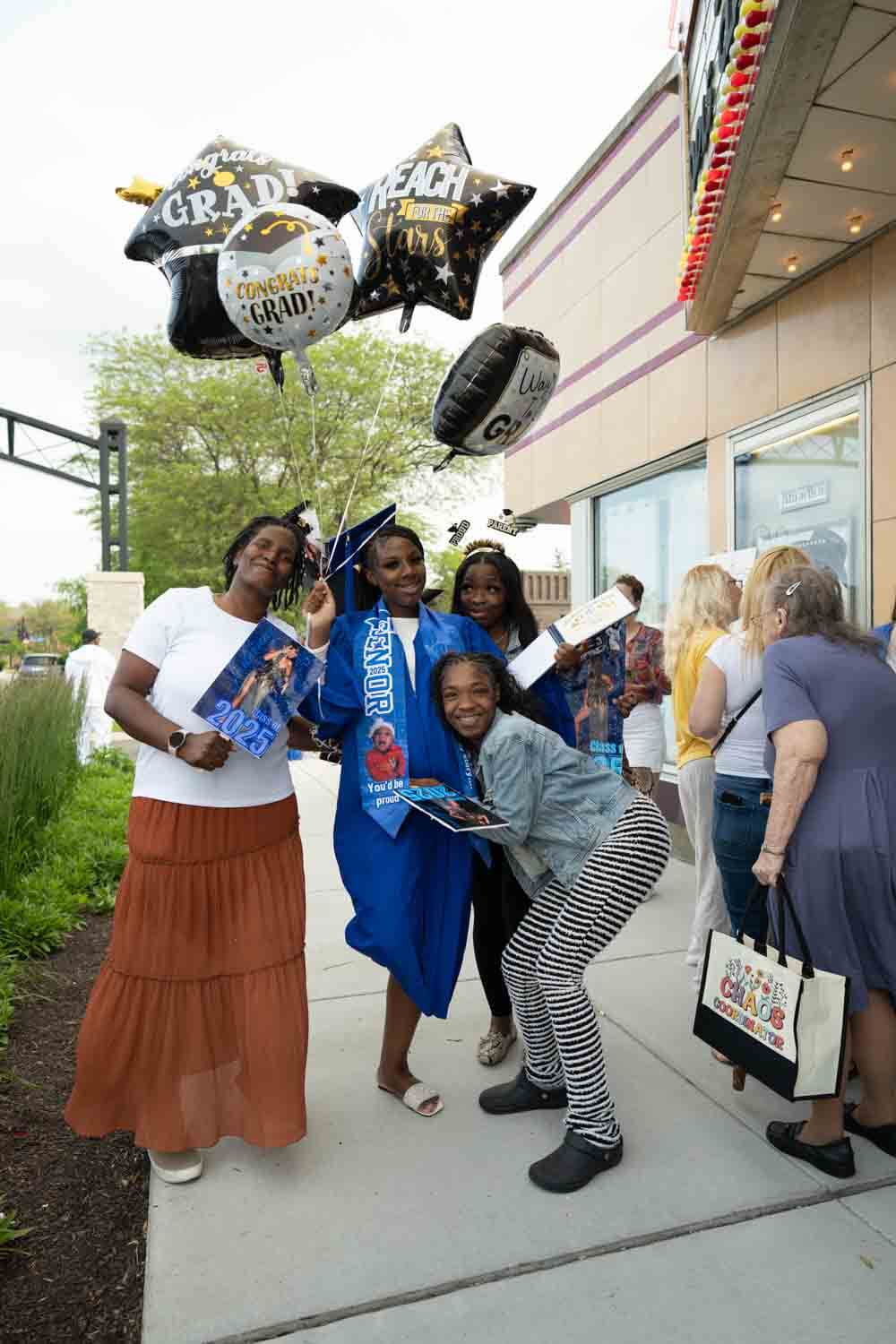 A graduate in a blue cap and gown holds celebratory balloons